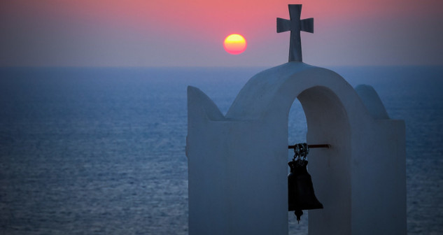 Chapel with cross and bell with a sunset over the sea in the background